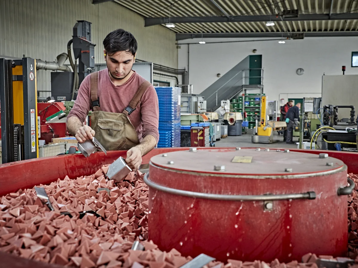 Mitarbeiter an einer Gleitschleifanlage mit Metallbauteilen und Schleifkörpern